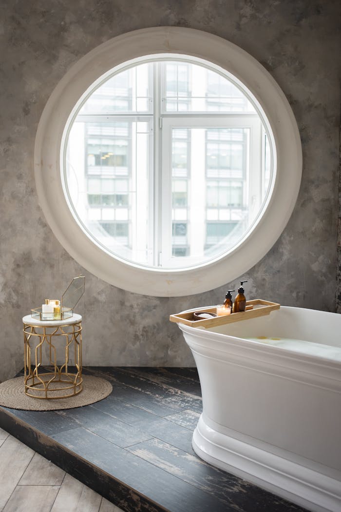 The Art of Drawing Readers In: Your attractive post title goes here Interior of contemporary bathroom with white bathtub and small table placed against concrete wall with round window in daylight